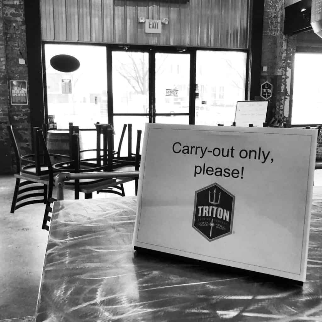 An photo of Triton Brewing Company's empty tasting room with a sign reading carry-out only please